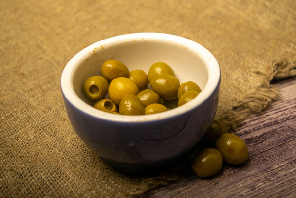 Olive verdi in una ciotola di ceramica su uno sfondo di iuta grossolana. Da vicino. - Foto, immagini