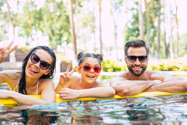 Handsome smiling man and cute excited woman with them little lovely daughter are having fun in summer swim pool while resting in hotel. - Foto, Imagem