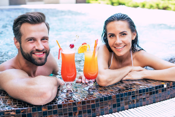 Cheerful couple in love are resting in a swimming pool while summer vacation. - Fotoğraf, Görsel