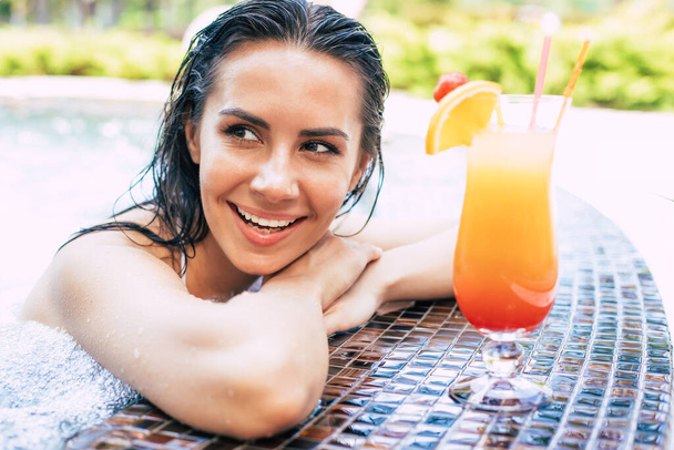 Beautiful excited smiling woman is relaxing in summer swim pool and drinks refreshing cocktail. - Fotoğraf, Görsel