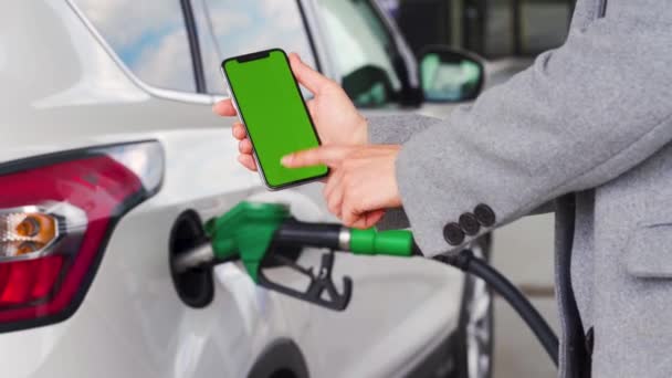 Γυναίκα χρησιμοποιεί μια εφαρμογή για κινητά σε ένα smartphone για να πληρώσει για τον ανεφοδιασμό ενός αυτοκινήτου. Smartphone με πράσινη οθόνη. Κλειδί χρωμίου - Πλάνα, βίντεο
