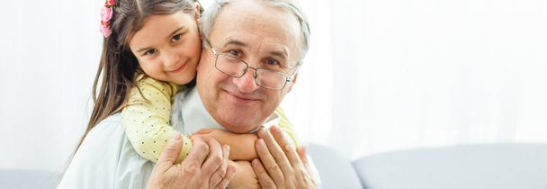 Το χαρούμενο κορίτσι αγκαλιάζει έναν παππού στον καναπέ. - Φωτογραφία, εικόνα