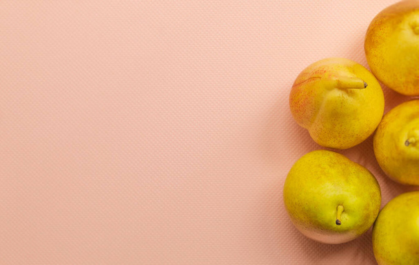 View from above on the ripe, overripe fruit that is placed on the pink background of the horizontal photograph. These are yellow pears. They are small, whole, in the peel - Photo, Image