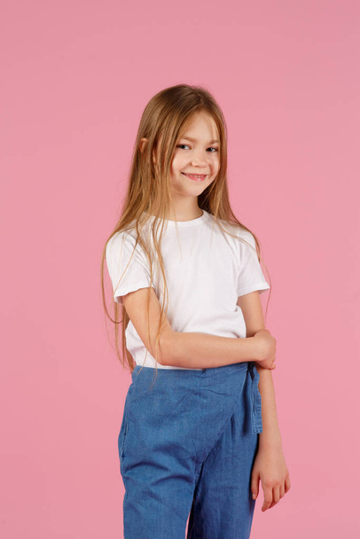 A little girl of 7 years in a white shirt on a pink background, emotions of joy and happiness. copy space - Foto, afbeelding