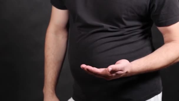Egy fekete rövidujjú pólós férfi egy tablettát ábrázol, ami eltűnik a gyomrából. - Felvétel, videó