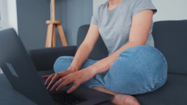 Woman sitting on a cozy sofa and working on a laptop. Concept of remote work. - Video