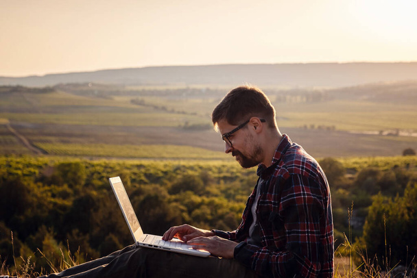 homem com laptop sentado à beira de uma montanha com vistas deslumbrantes sobre o vale. Conceito de cobertura de broaband de rede celular. 5G
. - Foto, Imagem
