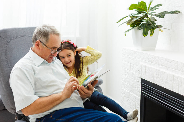 Внучка и дедушка смотрят вместе фотографии в фотоальбоме дома - Фото, изображение