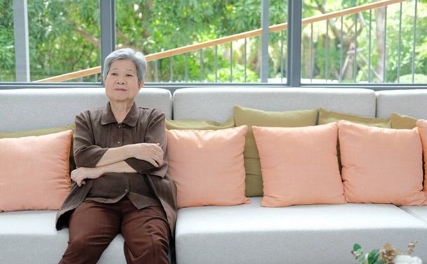 アジア系のおばあさんが家でソファでリラックスしてた。高齢者のレジャーライフスタイル - 写真・画像