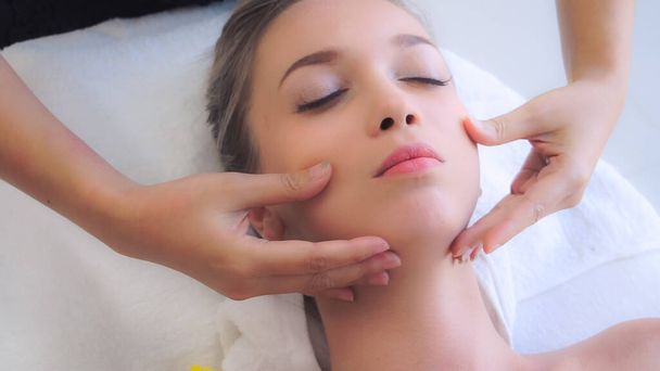 Relaxovaná žena ležící na lázeňském lůžku pro masážní ošetření obličeje a hlavy masážním terapeutem v luxusním lázeňském středisku. Wellness, stresová a omlazovací koncepce. - Fotografie, Obrázek
