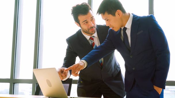 Two business people talk project strategy at office meeting room. Businessman discuss project planning with colleague at modern workplace while having conversation and advice on financial data report. - Photo, Image