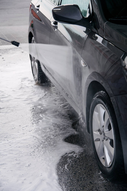 Detergent is washed off with water from the side of the gray car at the sink - Photo, image
