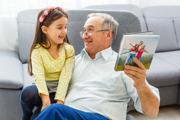 Внучка и дедушка смотрят вместе фотографии в фотоальбоме дома - Фото, изображение