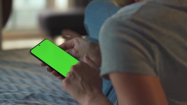 Mujer en casa acostada en un sofá y usando un smartphone con pantalla verde en modo vertical. Chica navegando por Internet, viendo contenido, videos, blogs. POV. - Imágenes, Vídeo