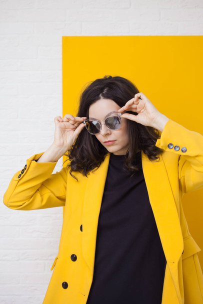 stylish and daring young brunette in a bright yellow jacket and mirrored sunglasses. - Valokuva, kuva