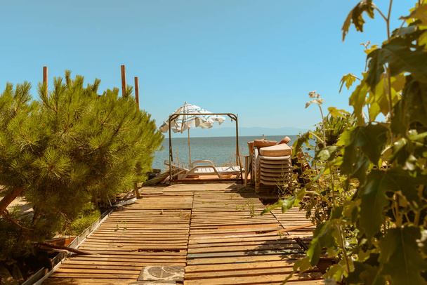 парасолька літнього пляжу та стільці на палубі, що стоять бездіяльно біля моря на дерев'яній платформі
 - Фото, зображення