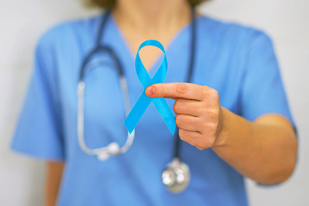Female doctor or surgeon holds a blue ribbon, closeup. Cancer Awareness Concept - Fotó, kép