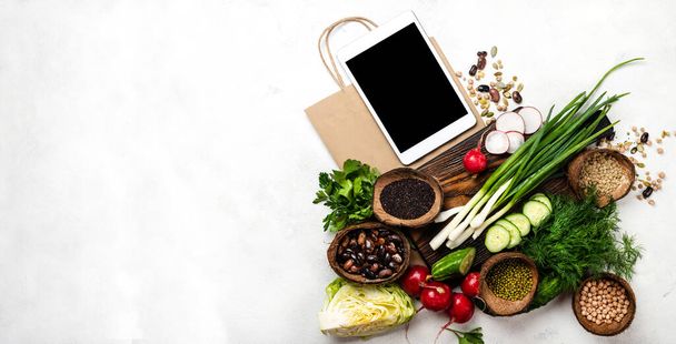Tabletcomputer en boodschappentas met ingrediënten voor het koken van gezond voedsel. Bovenaanzicht met plaats voor tekst. - Foto, afbeelding