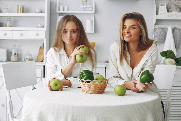 Beautiful and sporty girls in a kitchen with a vegetables - Фото, зображення