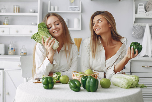 Beautiful and sporty girls in a kitchen with a vegetables - Photo, Image