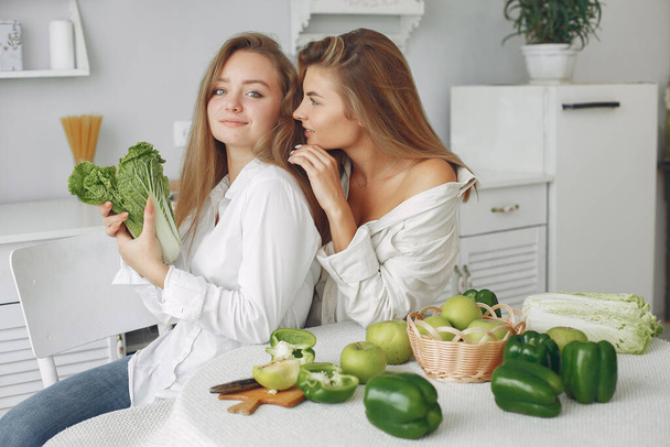 Beautiful and sporty girls in a kitchen with a vegetables - Foto, Imagem