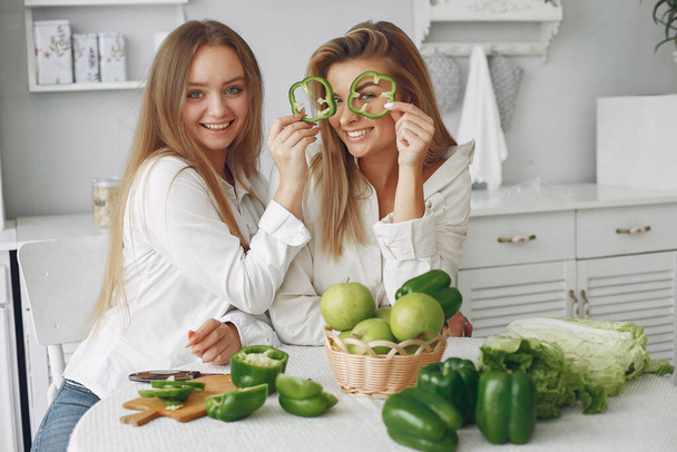Beautiful and sporty girls in a kitchen with a vegetables - Valokuva, kuva
