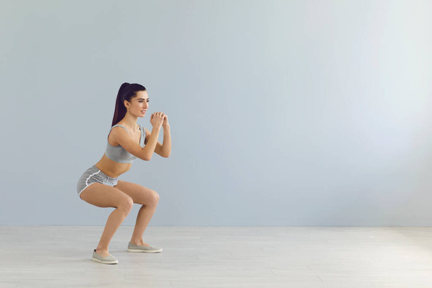 Fit sportswoman doing squats during workout near wall - Foto, immagini