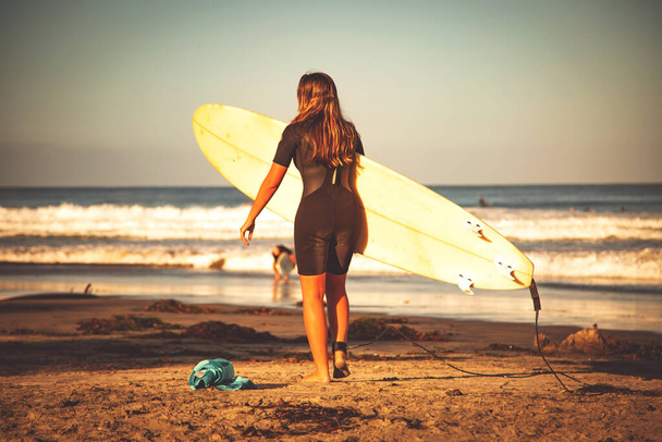 Chica surfista en una playa. Mujer en una playa yendo a surfear, llevando tabla de surf
. - Foto, Imagen