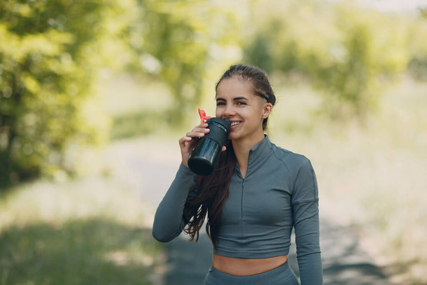 Moe runner vrouw jogger drinken gebotteld water na joggen in park outdoor. - Foto, afbeelding