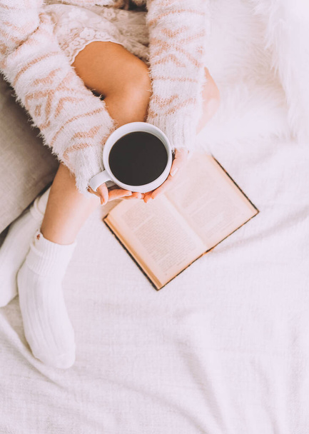 Young woman on the bed with old book and cup of coffee enjoys her stay. - Foto, imagen