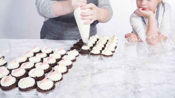 Крок за кроком. Маленька дівчинка допомагає прикрасити міні шоколадні кекси шоколадними сніжинками
. - Фото, зображення