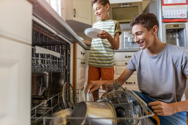 Two boys loading the dishwasher together at home - Photo, Image