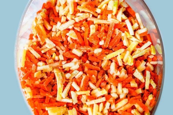 Un mucchio di verdure surgelate (carota, prezzemolo e sedano) tagliate a pezzetti sottili (julienne) in una ciotola di vetro, vista dall'alto. - Foto, immagini