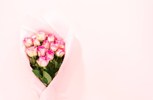 Flat lay. Bouquet of fresh pink roses wrapper in a pink paper on a pink background. - Foto, immagini