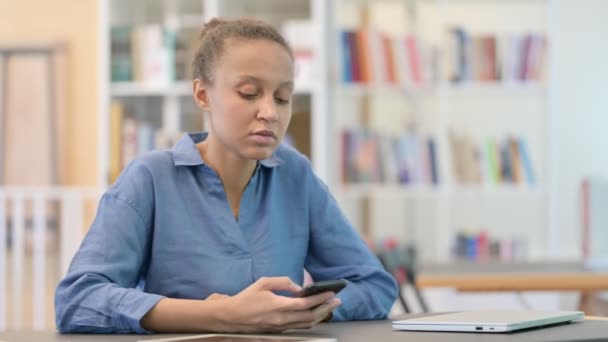 Donna africana annoiata che scorre sullo smartphone in biblioteca - Filmati, video