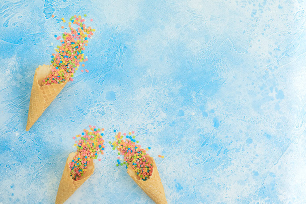 Dulces de confeti brillantes con cono de gofre en azul. Piso tendido, vista superior
 - Foto, imagen