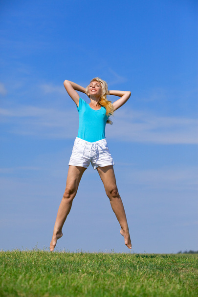 Pretty young woman jumping on green grass against brightly dark blue sky - Photo, Image