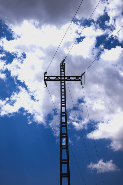 農村部に電気を運ぶ高電圧ケーブルをサポートする電気タワーのイメージ。背景には青い空に浮かぶ雲が - 写真・画像