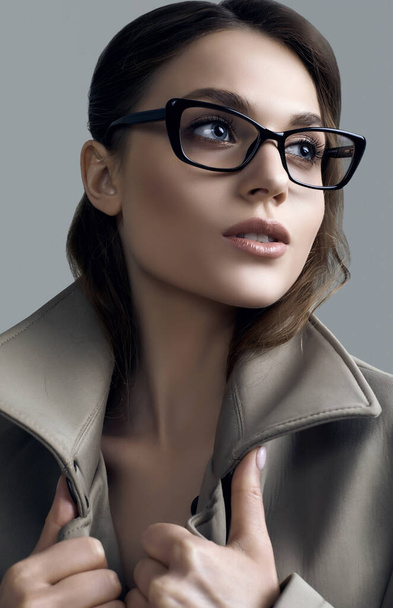 若いです美しいですヒップスター女性の肖像でファッショナブルなコートと眼鏡上のダークグレーの背景にスタジオ - 写真・画像