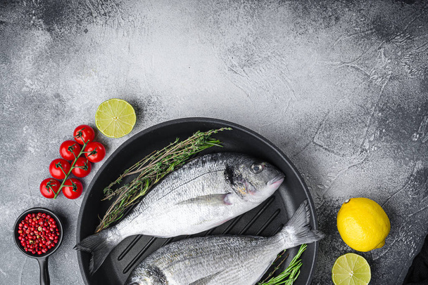 Rauwe zeebrasem of dorado rauwe vis op grill pan met ingrediënten op grijs witte textuur achtergrond, bovenaanzicht met ruimte voor tekst - Foto, afbeelding