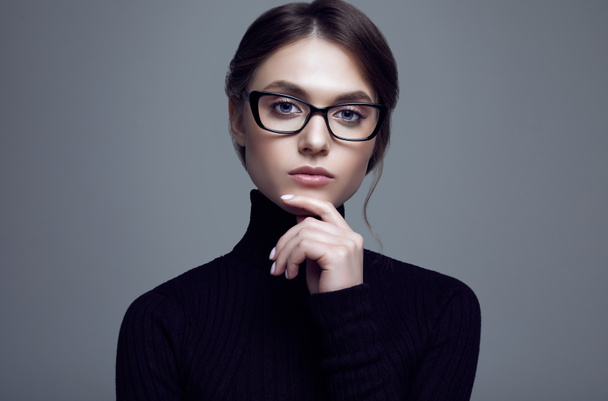 Retrato de una linda estudiante con suéter de cuello alto negro y gafas con estilo posando sobre fondo gris en el estudio
 - Foto, imagen