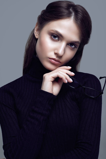 Портрет милої студентської дівчини в чорному светрі і стильних окулярах, що позують на сірому фоні в студії
 - Фото, зображення
