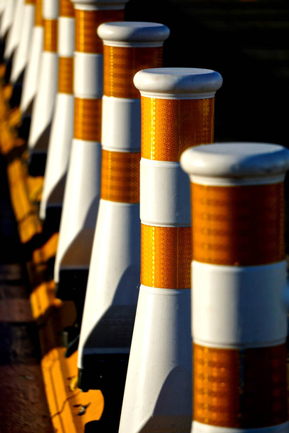 Крупный план ряда белых разделителей полос безопасности дорожного движения с оранжевыми отражателями, при ярком солнечном свете. - Фото, изображение