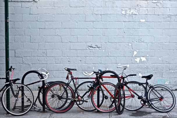 Brooklyn, New York: Egy csoport kerékpár láncra verve aláírni oszlopok és járdaszegély kerékpár áll egy városi járdán, szürke festett téglafal a háttérben. - Fotó, kép