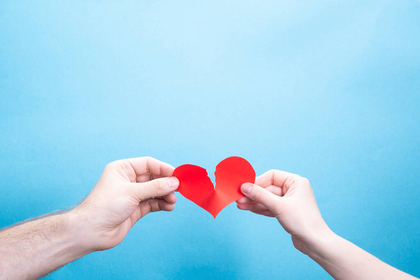Female and male hand break a paper red heart on a blue background with place for text. Relationship problems - Foto, Imagem