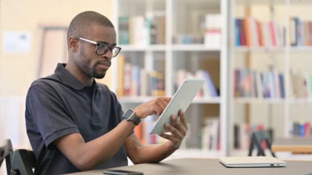 Junger Afrikaner benutzt Tablet in Bibliothek - Filmmaterial, Video