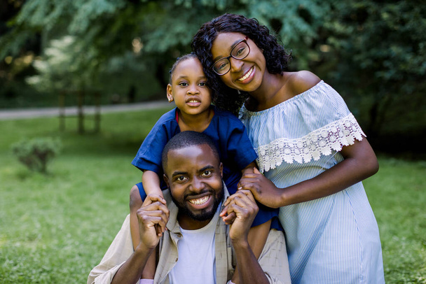 Family outdoor recreation, happy family in love concept. Joyful attractive african family playing in the park. Mother, father and little daughter having picnic at summer park - Fotografie, Obrázek