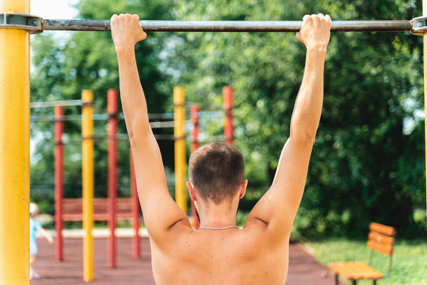 The athlete pulls himself on the horizontal bar. Doing sports in the park. Teip on the back and neck, curvature of the spine, scoliosis, back problems - Фото, зображення