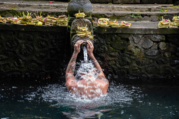 Zachodni człowiek kąpiący się wodą święconą według wyznania hinduskiego z wiarą w świątynię na Bali, Indonezja - Zdjęcie, obraz