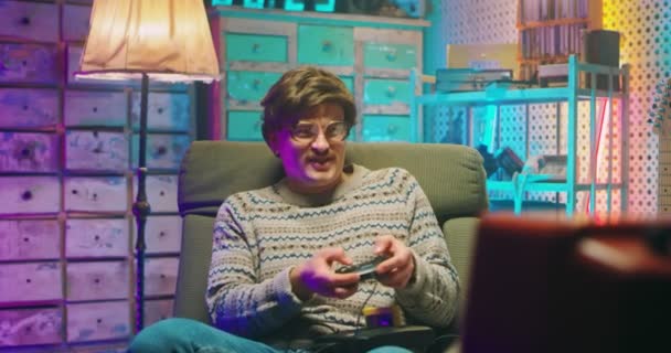 Kaukasischer Nerd mit Brille und Schnurrbart sitzt vor einem alten Fernsehbildschirm und spielt Videospiele mit Joystick. Männliche Dummköpfe verlieren im Spiel. Retro-Stil der 80er Jahre. Verlierer aus den 90er Jahren - Filmmaterial, Video